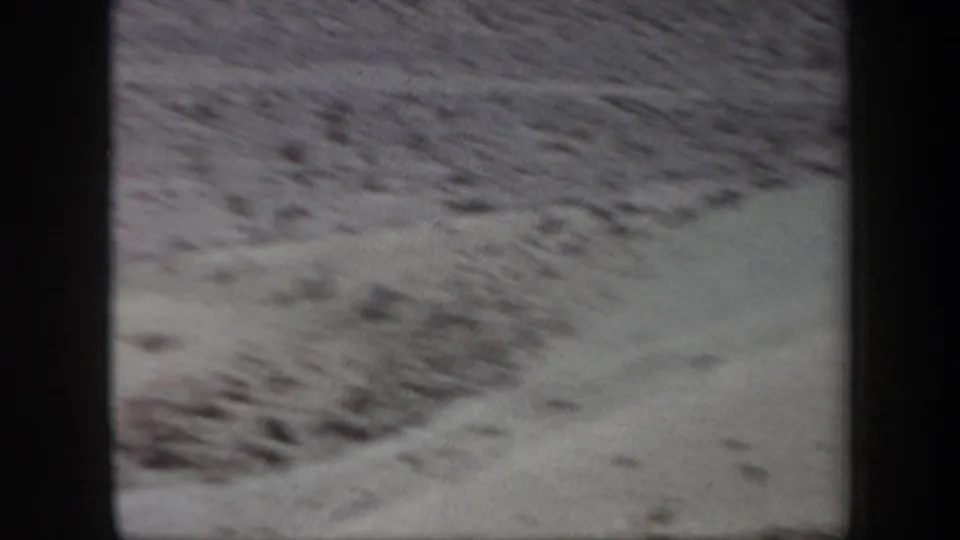 1957 Arizona 8mm frame showing a soft, close view of barren desert ground with scattered low scrub and heavy gate shadowing.