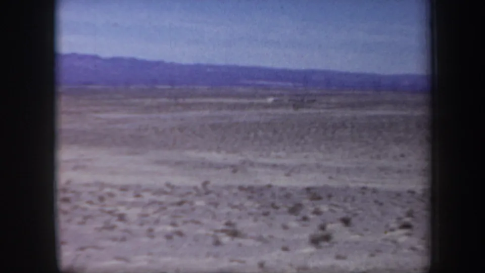 1957 Arizona 8mm frame showing a broad desert basin with sparse vegetation and a long mountain range in the distance.