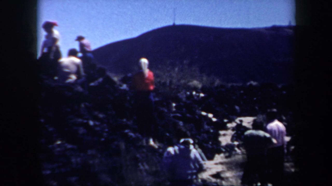 1957 Arizona 8mm frame showing people scattered across a rugged hillside with distant slopes and strong film vignetting.