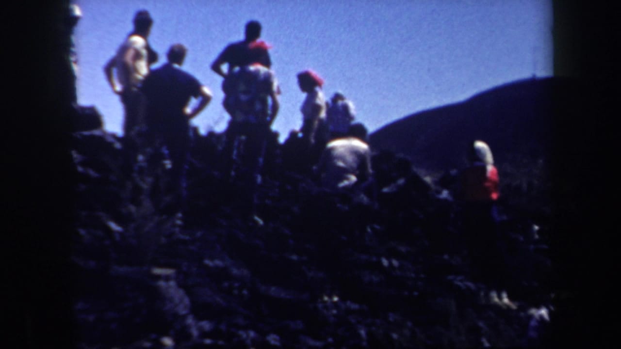A home-movie frame shows adults gathered on uneven rocky terrain in Arizona, with silhouetted figures, hats, and distant hills.