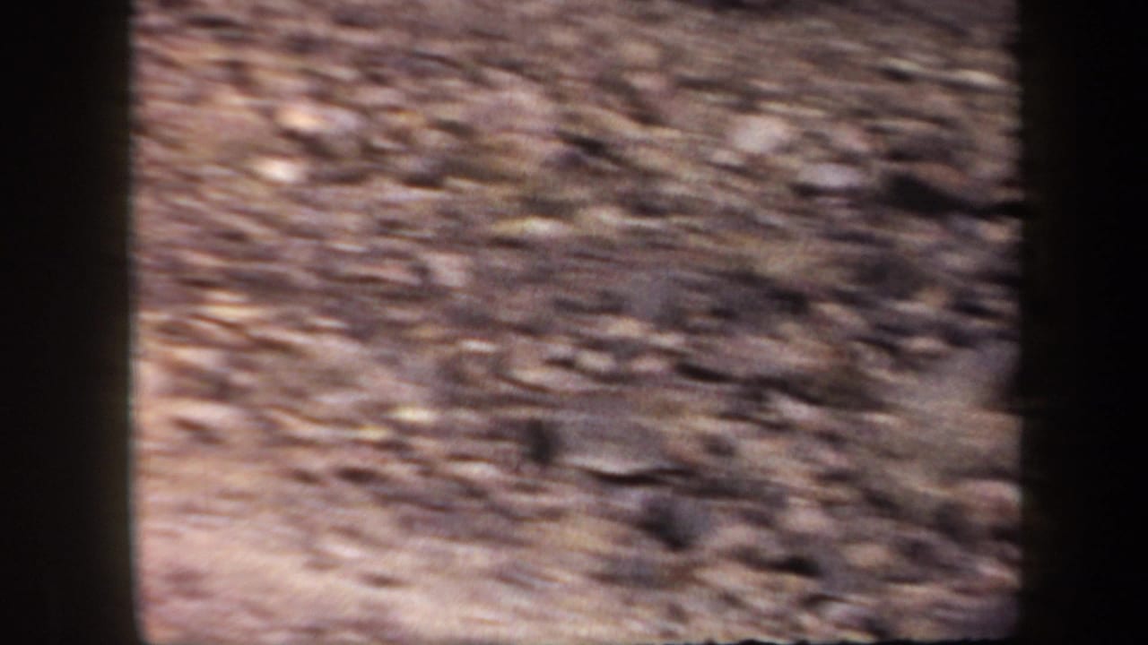 Soft, handheld 1957 Arizona 8mm view of rocky desert mountain ground and slope during a hiking sequence.