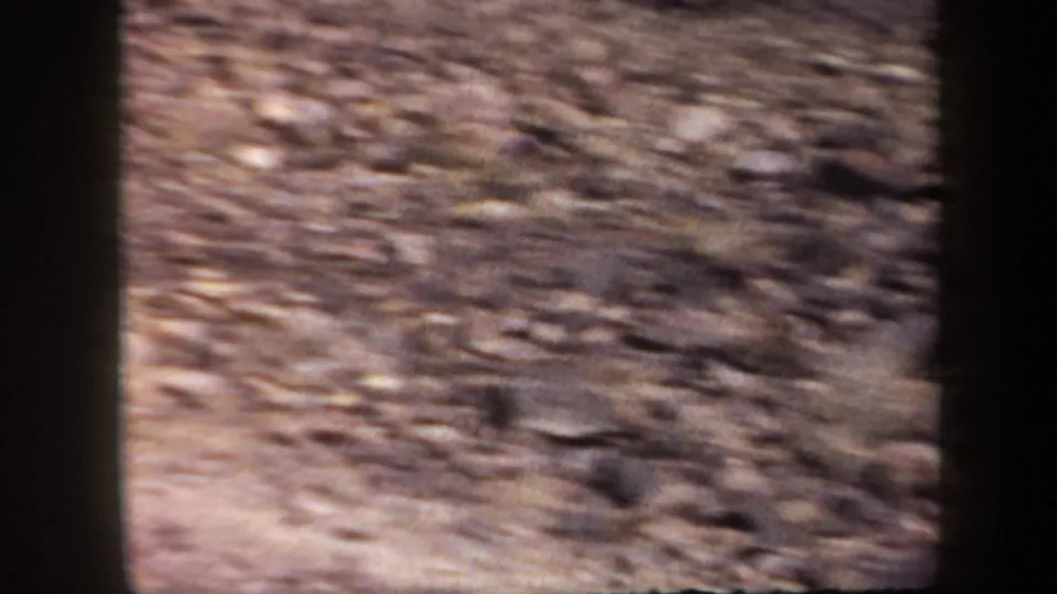 Soft, handheld 1957 Arizona 8mm view of rocky desert mountain ground and slope during a hiking sequence.