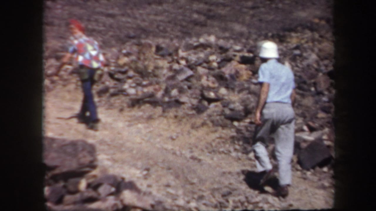 Two adult men hike up a rocky Arizona trail, one wearing a white bucket hat and carrying a dark bag.