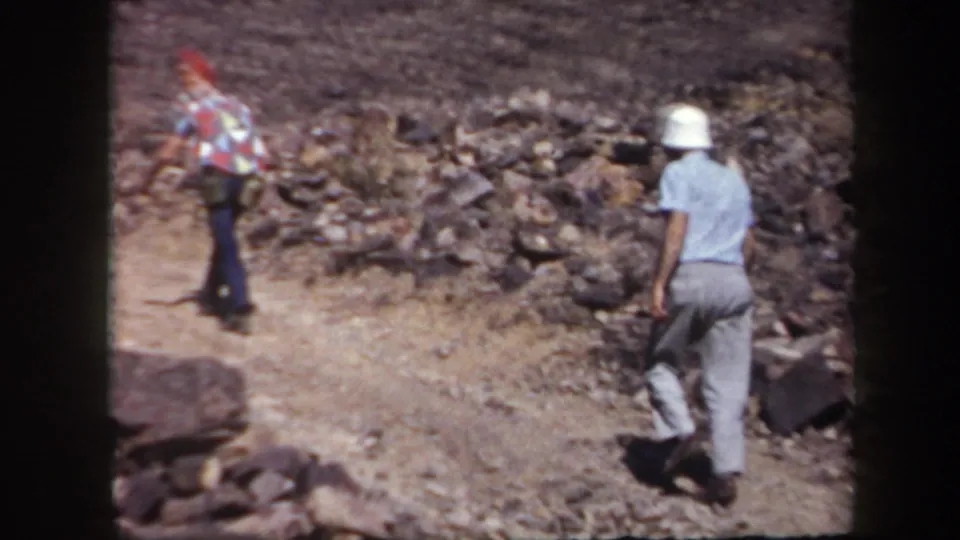 Two adult men hike up a rocky Arizona trail, one wearing a white bucket hat and carrying a dark bag.