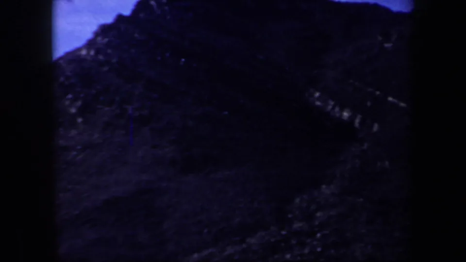 Underexposed 8mm frame shows a dark rocky mountain slope with a blue sky edge during the Arizona hiking sequence.