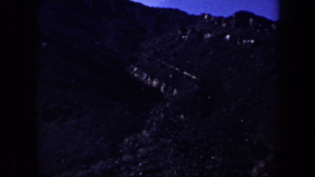 Dark rocky hillside beneath a deep blue sky, with soft focus and heavy shadow.