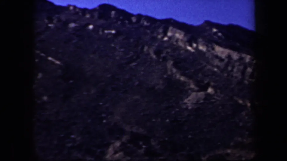 1957 Arizona home-movie frame of a rocky mountain slope with layered outcrops and heavy shadow.