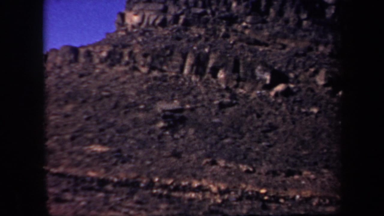 Rocky mountainside with jagged dark outcrops under a blue sky.