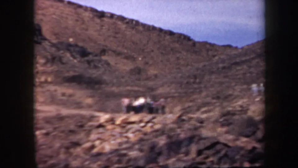 1957 Arizona 8mm frame showing adults on a rugged rocky hillside in an arid landscape.