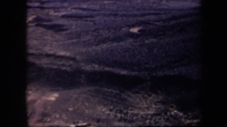 1957 Arizona home-movie frame showing dark, rocky desert ground with handheld 8mm texture.