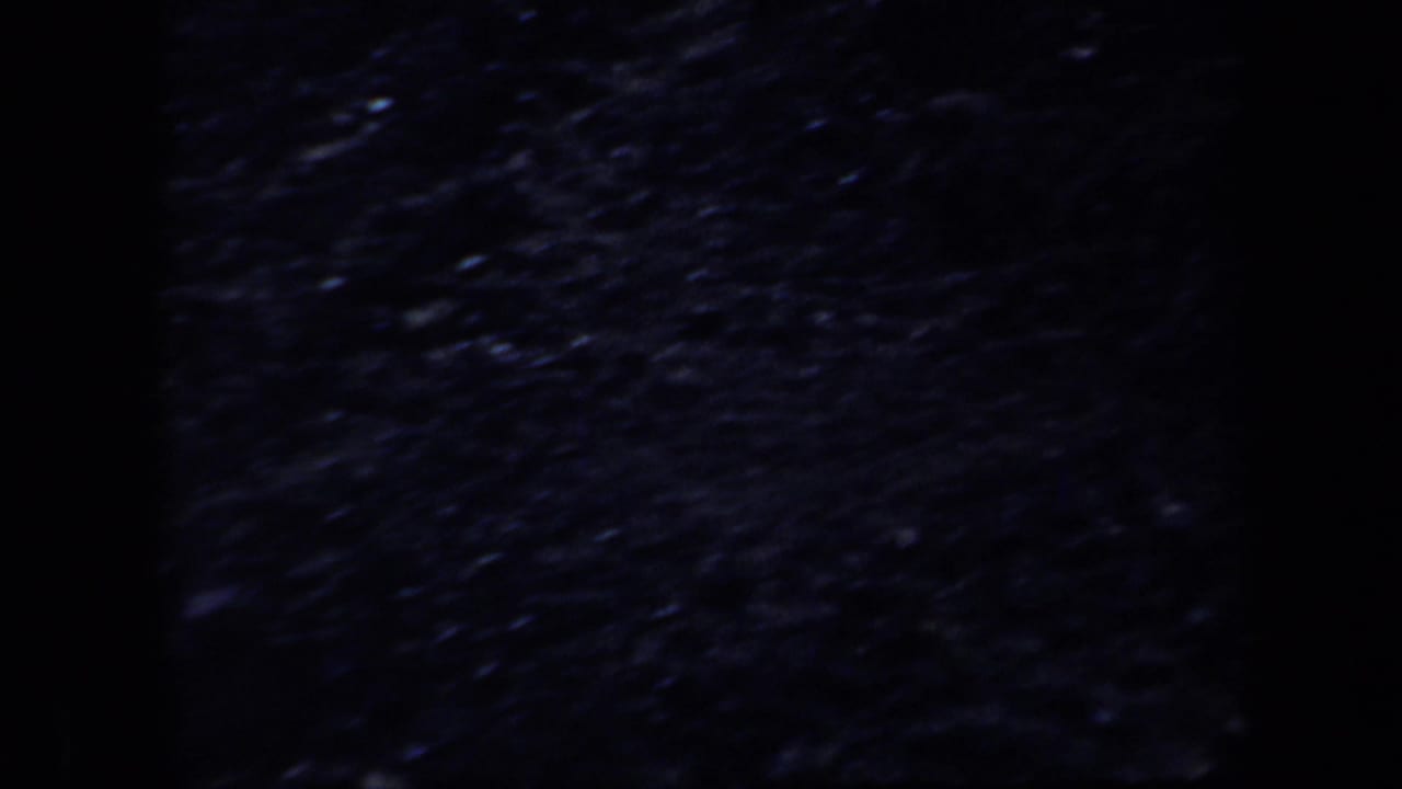 Dark, grainy close view of uneven rocky ground with a black vertical border.