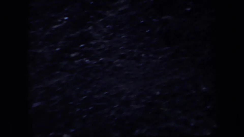 1957 Arizona 8mm frame showing underexposed rocky terrain with heavy grain and dark frame edges.