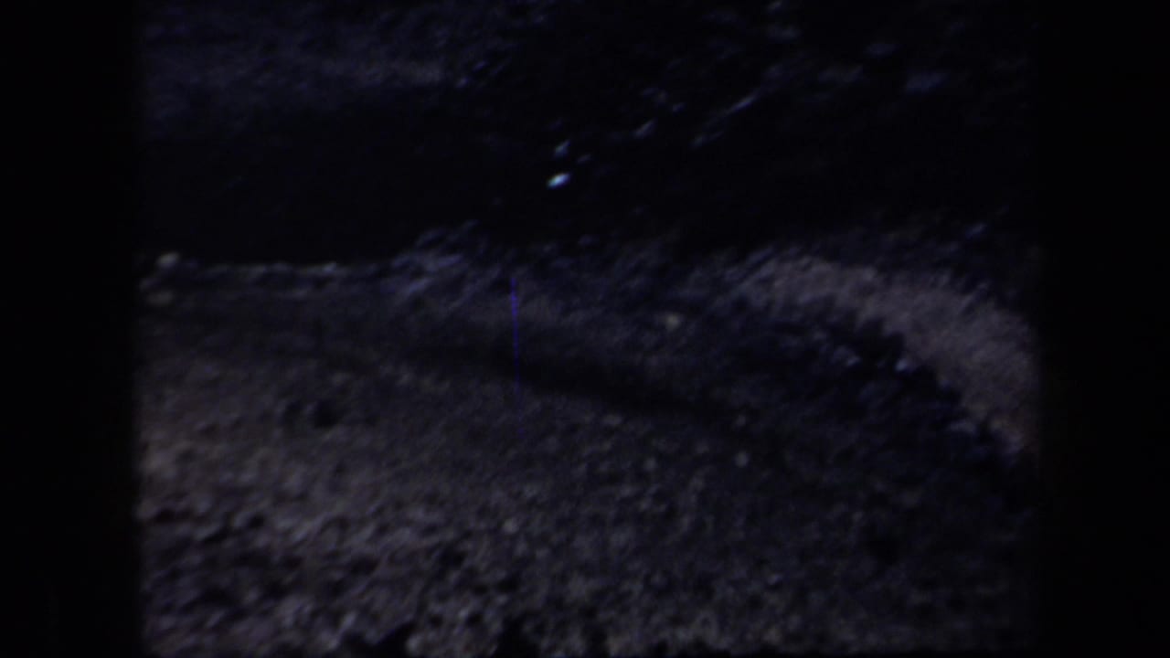 Underexposed 8mm view of rough Arizona terrain, with a curved raised edge and visible film grain.