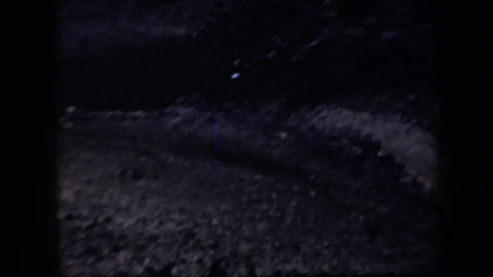 Underexposed 8mm view of rough Arizona terrain, with a curved raised edge and visible film grain.