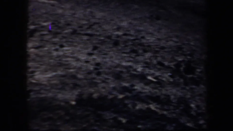 1957 Arizona home-movie frame of rough ground, marked by heavy grain and a vertical purple light leak.