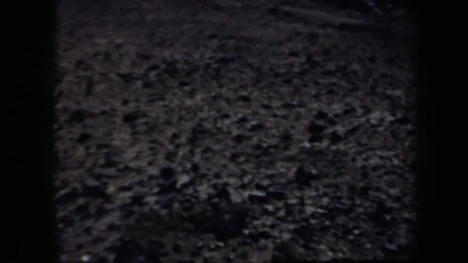 Underexposed 8mm frame of pebbled ground in Arizona, with dense grain and little visible horizon detail.