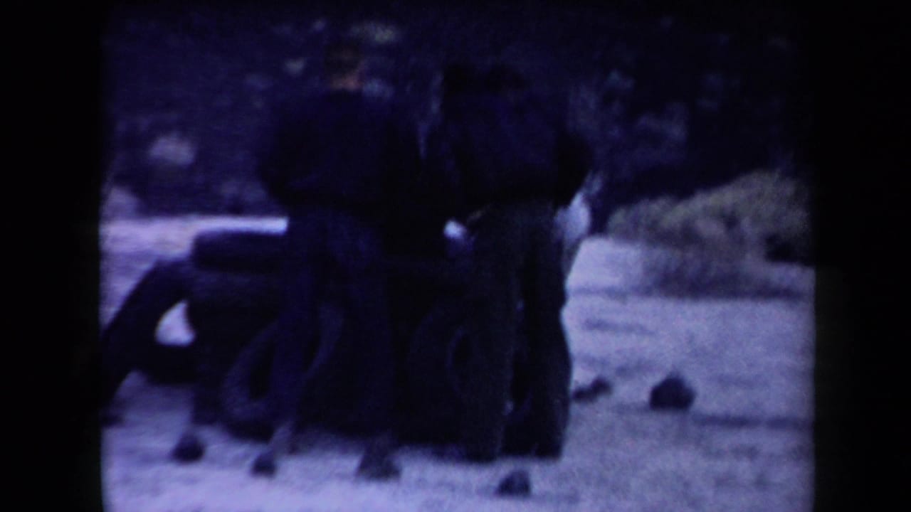 Three men stand around a low stack of tires on pale desert ground.