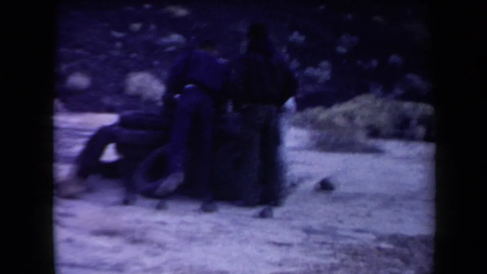 Two men stand near the tire stack while another figure is lower beside it in the 1958 Arizona desert home movie.