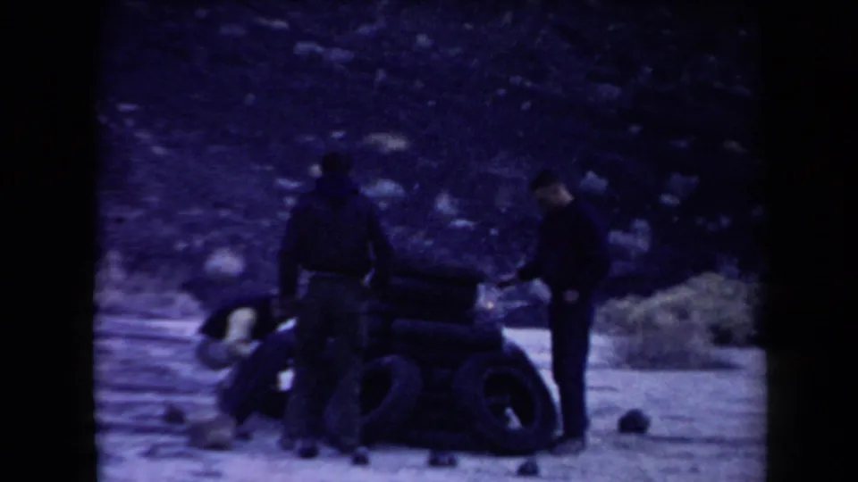 Three men cluster around a taller stack of tires, with one reaching toward the pile in the arid Arizona setting.