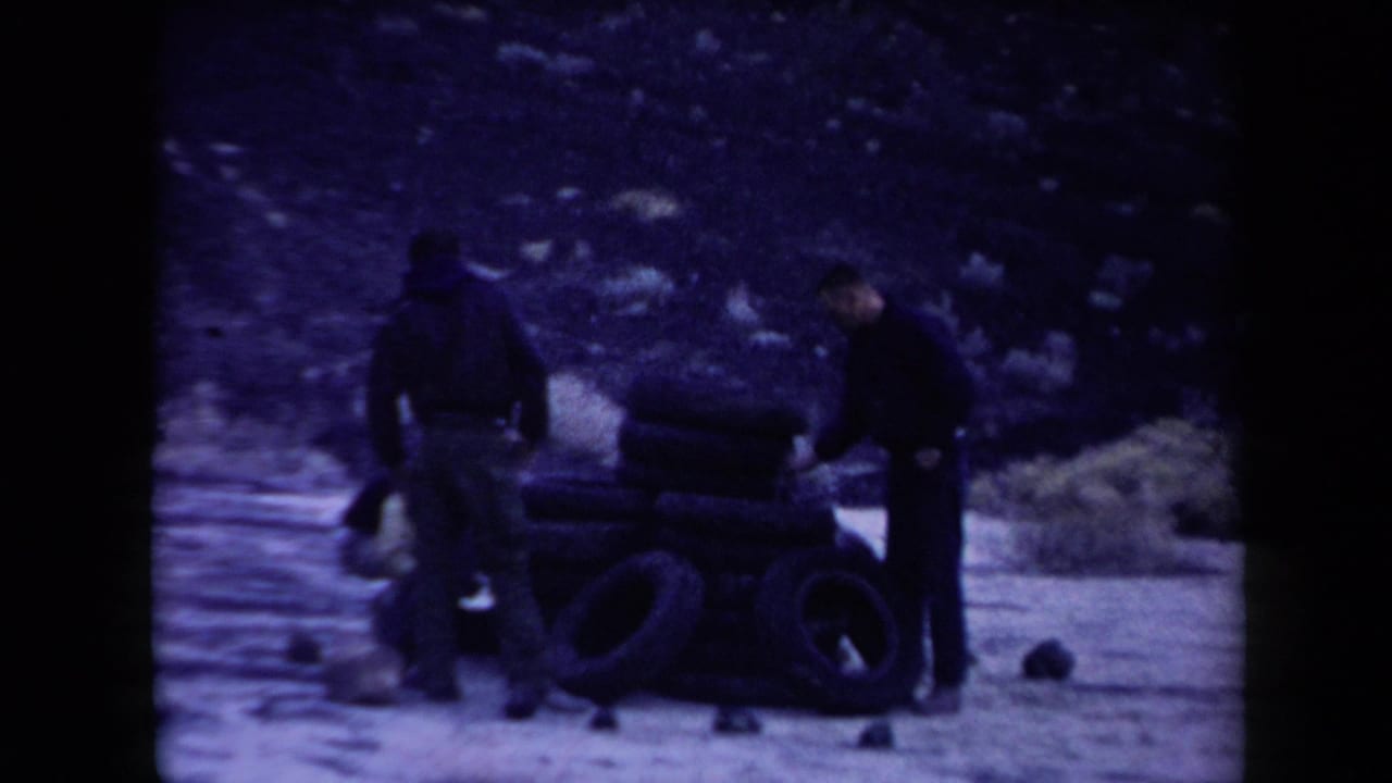 Three men stand around a stack of tires on sandy desert ground.