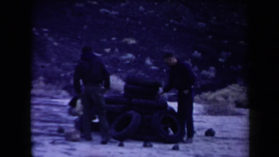 1958 Arizona home-movie frame showing three men around stacked rubber tires in a scrubby arid landscape.