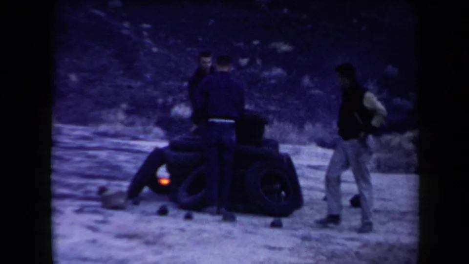 The men remain around the tire pile as a small flame glows low against the dark rubber in the Arizona outdoor setting.