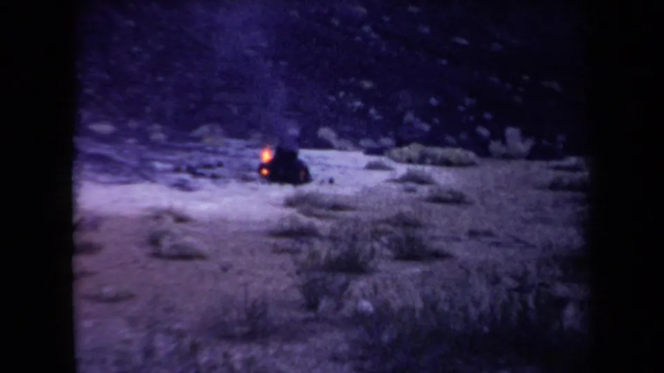 The final 8mm frame pulls back to a wider Arizona desert view where flames flicker from the tire pile amid scrub and rocky ground.