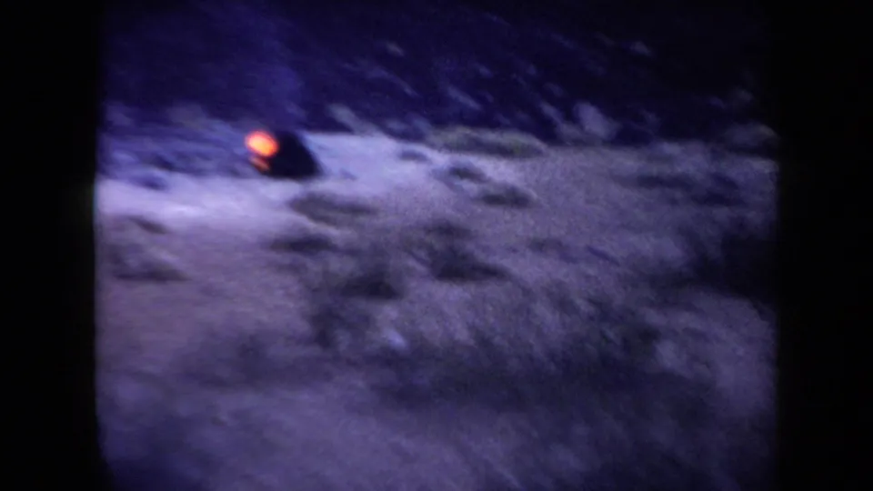 1958 Arizona 8mm frame showing dark mountainous ground with a small orange glow and strong purple-blue film color shift.