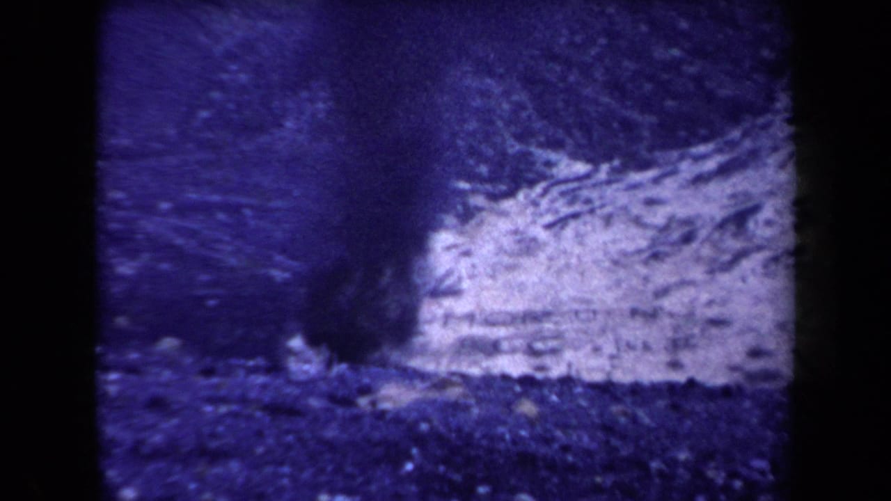 1958 Arizona 8mm frame with pale smoke or ash near dark mountain terrain, softened by grain and color fading.