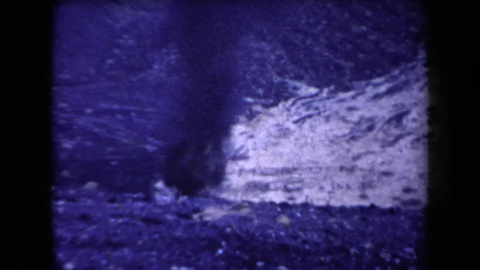 1958 Arizona 8mm frame with pale smoke or ash near dark mountain terrain, softened by grain and color fading.