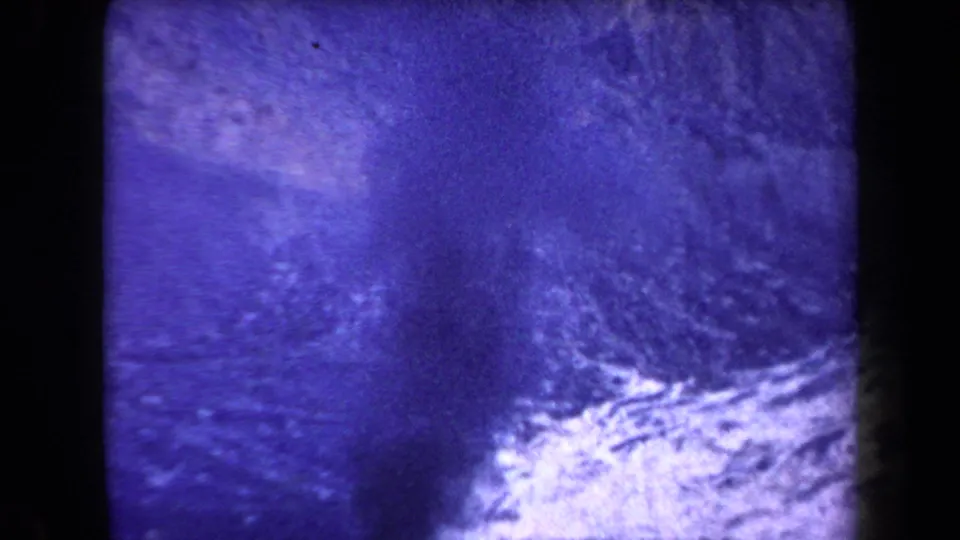 1958 Arizona 8mm frame showing a dark plume or shadow over pale rough ground, with strong grain and color shift.