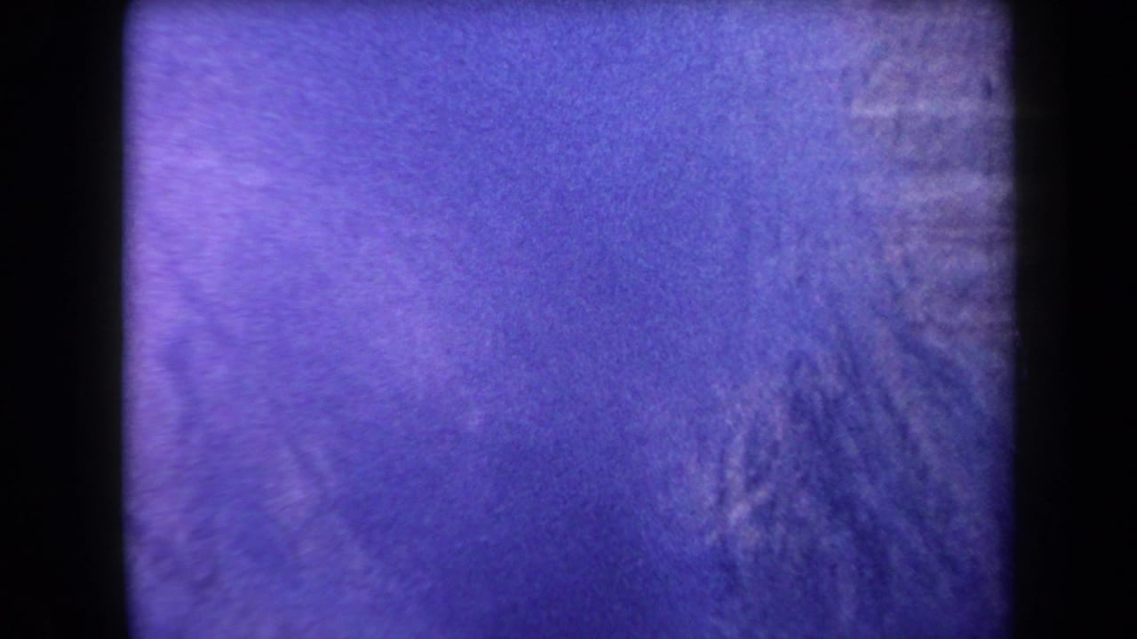 1958 Arizona 8mm frame showing a distant ridge with faint smoke and strong purple color shift from aged film stock.