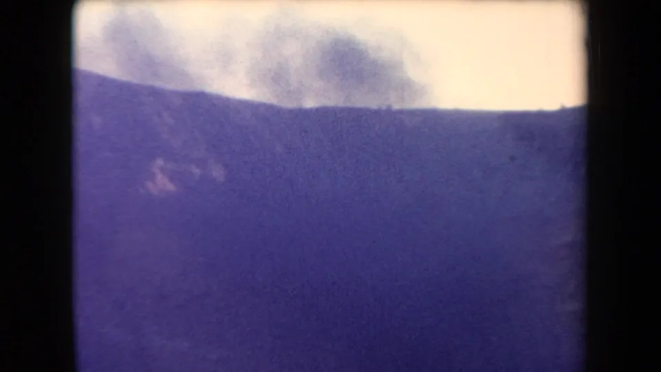 1958 Arizona 8mm still showing smoke over a distant ridge, with possible snow or light-toned ground on the slope.