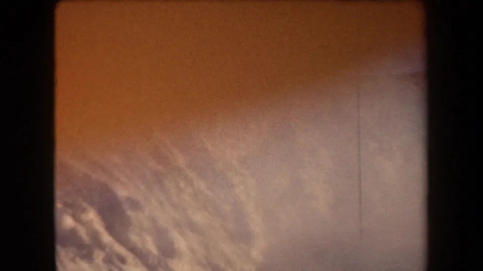 Aged 8mm frame from Arizona in 1958 showing rugged terrain, orange color shift, and haze or smoke along a sloped landscape.