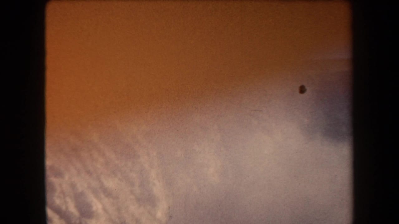 1958 Arizona 8mm frame showing an orange sky with pale cloud texture, soft exposure, grain, and dark gate edges.