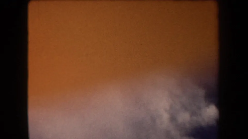 1958 Arizona 8mm frame with gray-white cloud forms against a warm orange sky and dark rounded film edges.