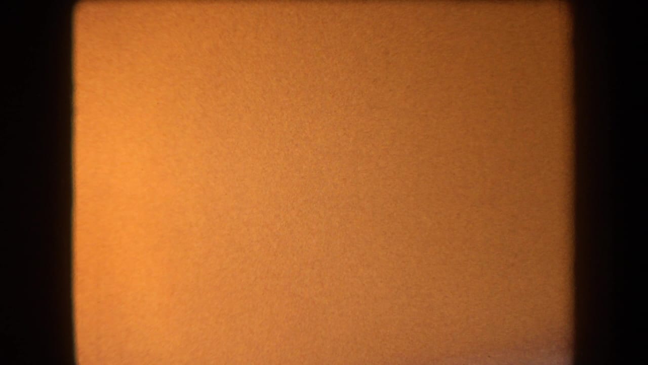 Warm orange blurred 8mm frame with dark vertical edges and grain.