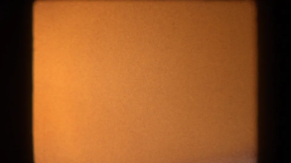 1958 Arizona 8mm frame showing an indistinct orange field with dark edge shadowing, soft focus, and visible film grain.