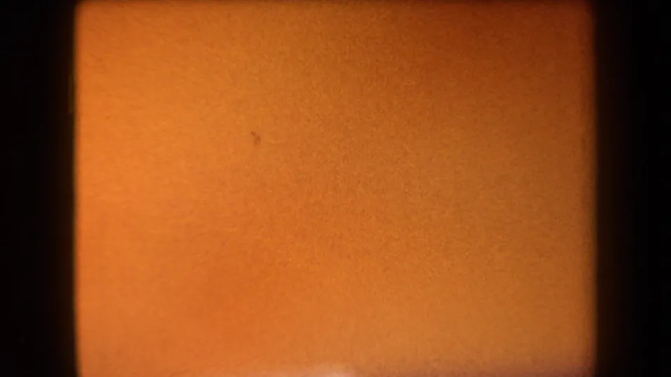 1958 Arizona 8mm frame showing an indistinct orange field, dark side border, granular texture, and a small mark near the left side.