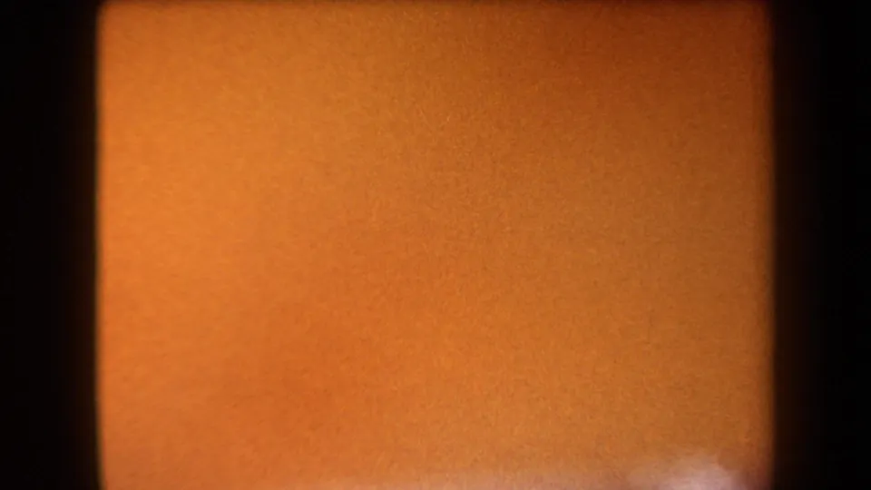 1958 Arizona 8mm frame with a soft orange field, dark vertical edge shadows, heavy grain, and no identifiable subject.