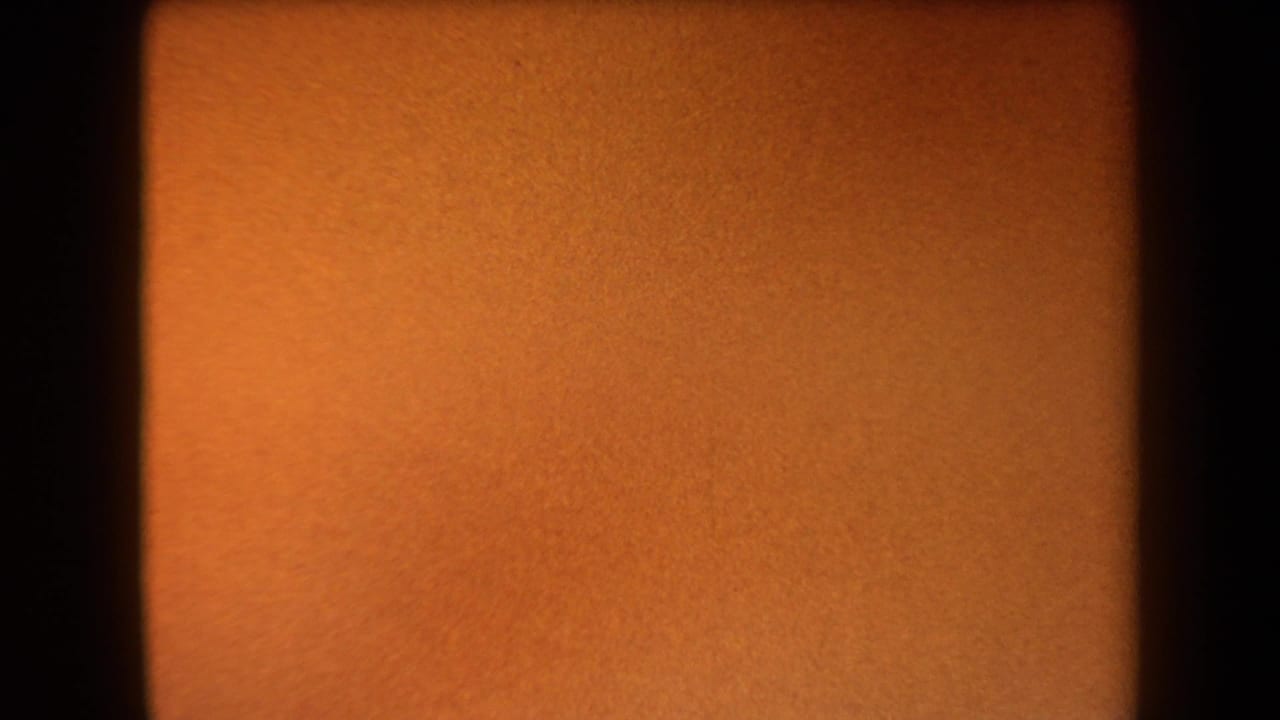 Warm orange 8mm leader fills the frame, with dark borders and fine grain preceding the Arizona canyon view.