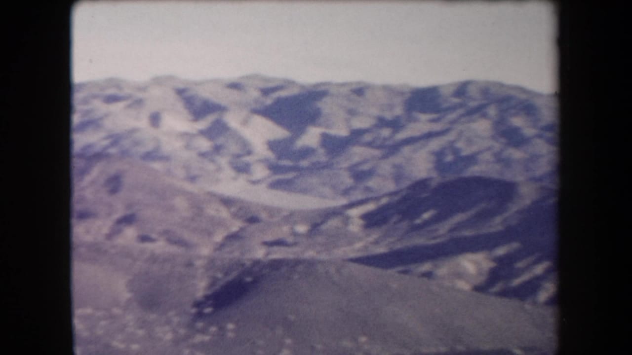 1958 Arizona 8mm frame with rolling desert mountains, a basin-like slope, and faded color from the home-movie scan.