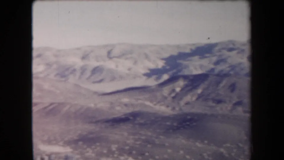 1958 Arizona home-movie frame showing dry foreground terrain and a distant mountain ridge through faded, soft 8mm imagery.