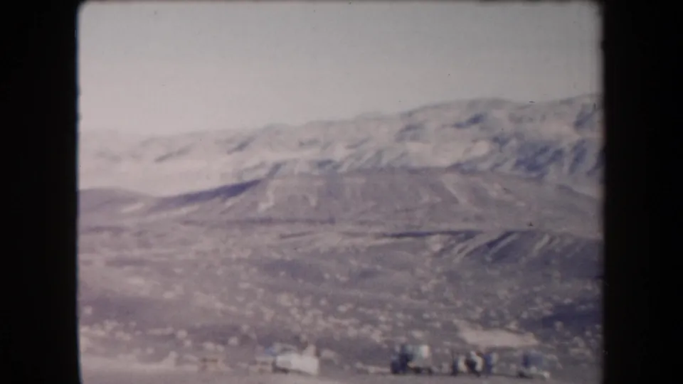 1958 Arizona 8mm frame of desert mountains with small distant figures or objects near the bottom edge of the scene.