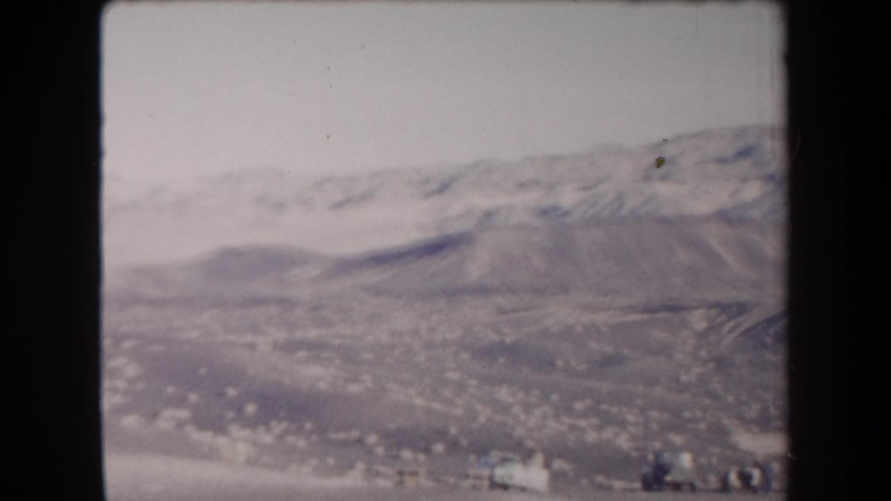 1958 Arizona 8mm frame showing a gray desert valley, far mountains, and small pale structures under a hazy sky.