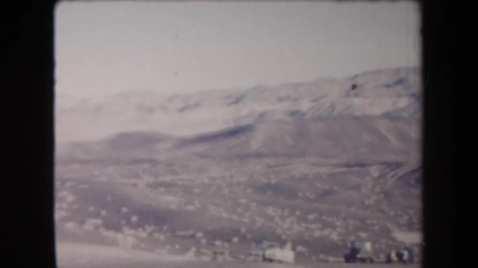 1958 Arizona 8mm frame showing a gray desert valley, far mountains, and small pale structures under a hazy sky.