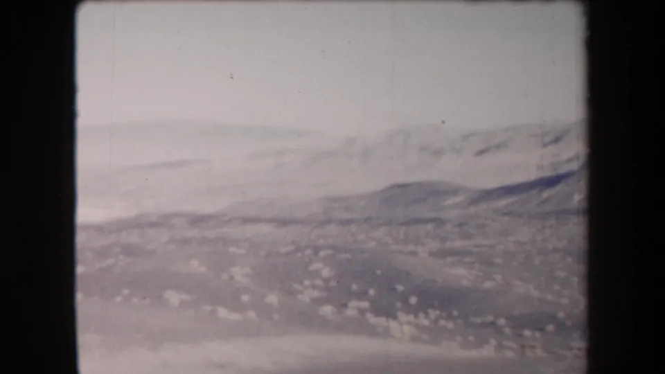 1958 Arizona home-movie frame with a broad, pale desert floor and low distant mountains softened by haze.