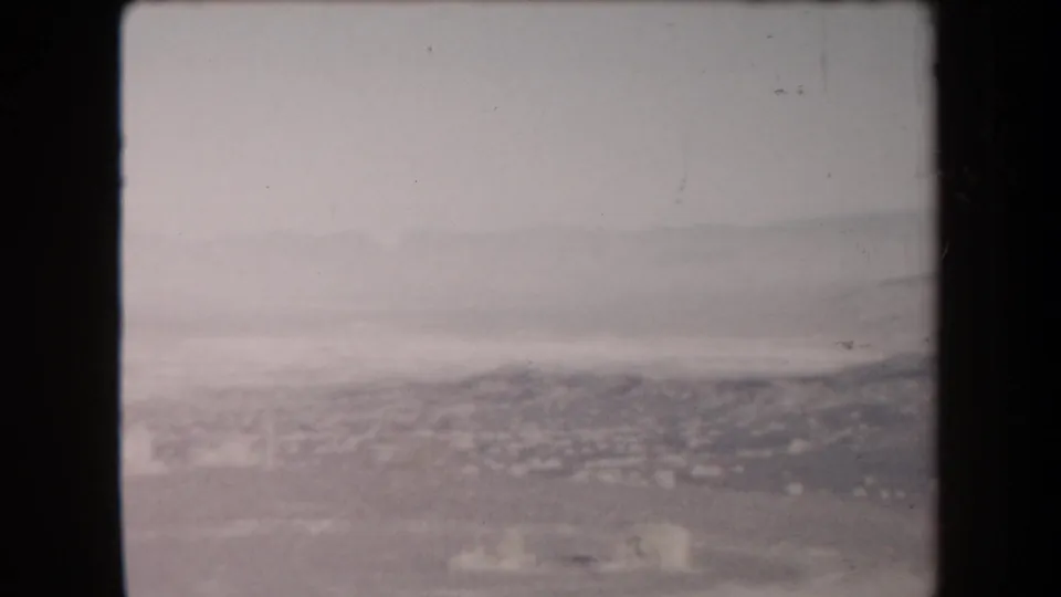1958 Arizona frame showing a distant desert valley and low mountain forms through a washed gray haze.