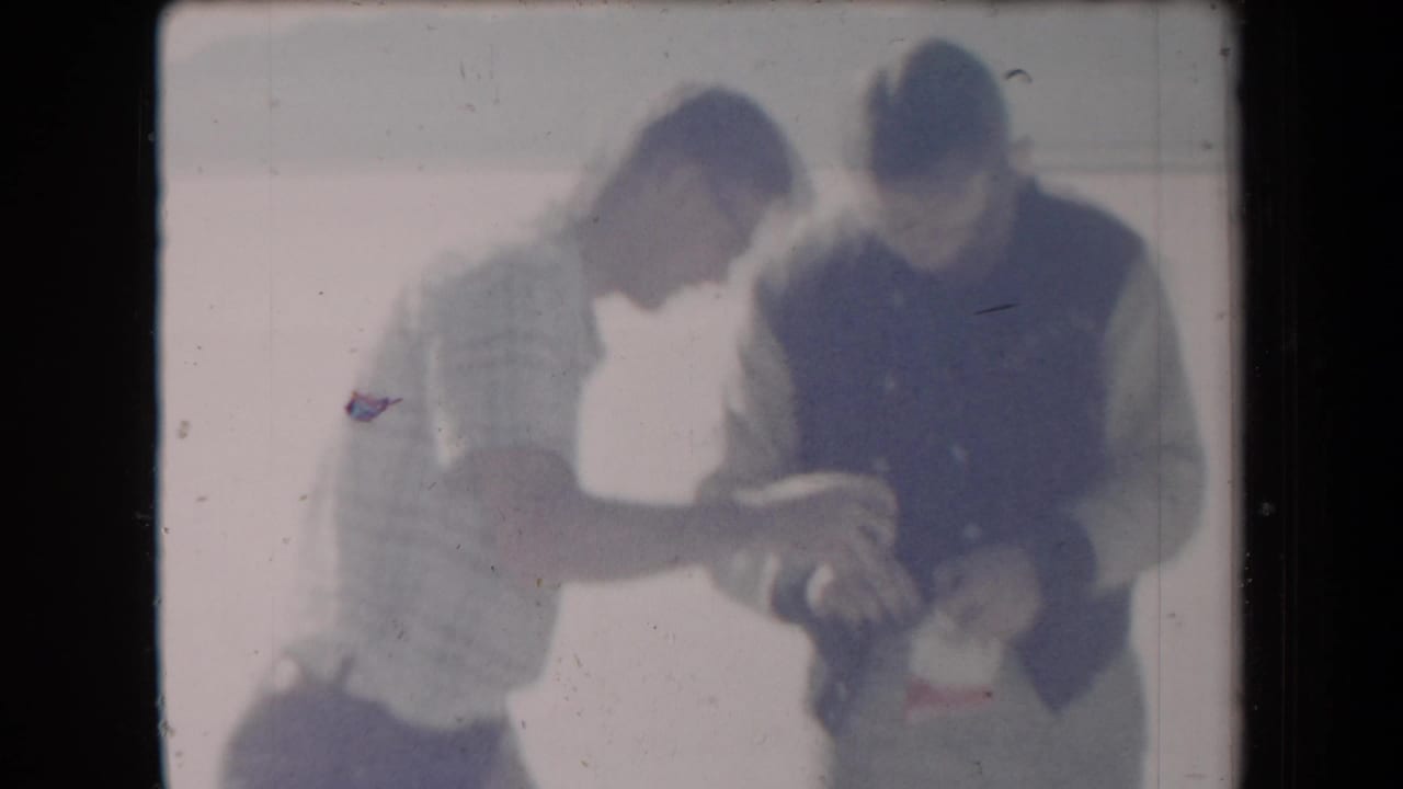 Two men stand close together outdoors, looking down at an object in their hands.