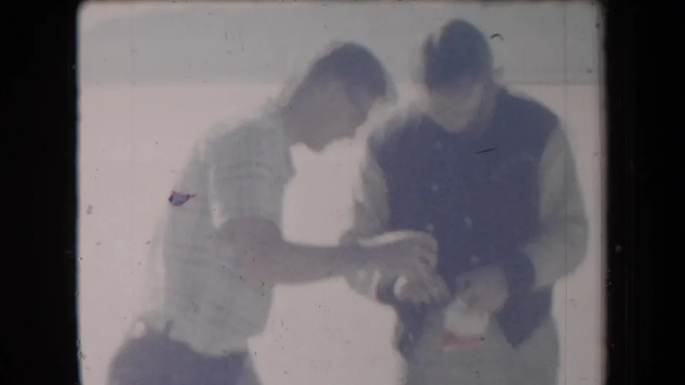 Two men in casual 1950s-style clothing appear to examine an object together in a bright Arizona desert setting.